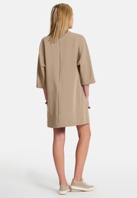 Beige, polven mittainen mekko, jossa on rento malli, leveät hihat ja takasaumadetaili. Yhdistetty vaaleisiin lenkkarisaappaisiin. Sulava rakenne.
