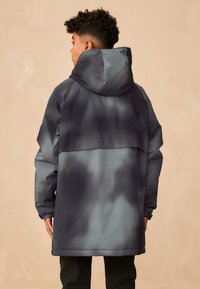 Veste résistante à l'eau en dégradé de gris, comprenant une capuche, des manches longues, des poignets élastiques et une coupe décontractée avec un grand panneau arrière.