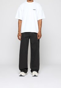 T-shirt blanc oversize avec un petit logo, associé à un pantalon large noir à motifs et des baskets de couleur claire.