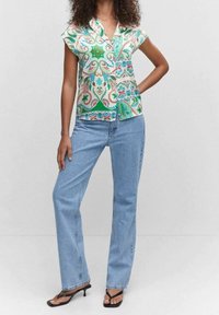 Camisa de manga corta con un colorido patrón floral, que incluye verde, azul y rojo, combinada con jeans rectos de mezclilla azul claro y sandalias negras.