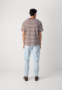 Brun og hvitstripet kortermet t-skjorte, løs passform, med lyseblå jeans. Brune sko fullfører det uformelle antrekket.