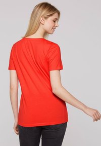 Czerwony t-shirt z krótkim rękawem o okrągłym dekolcie, wykonany z miękkiego materiału, z prostym krojem i minimalnymi detalami szwów na dole.