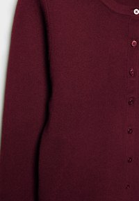 Cardigan en maille bordeaux avec un col arrondi, des manches longues, et une rangée de boutons assortis sur le devant. Texture douce.