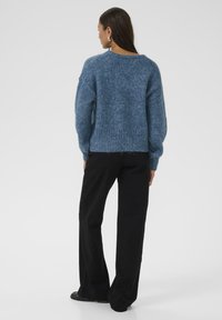 Maglione blu a maglia con una finitura testurizzata, orlo a costine e spalle cadenti, abbinato a pantaloni neri a gamba larga.