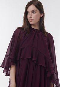 Lila Chiffonkleid mit hohen Kragen, geschichteter Rüsche an den Ärmeln und fließendem Stoff, der eine sanfte, elegante Silhouette schafft.