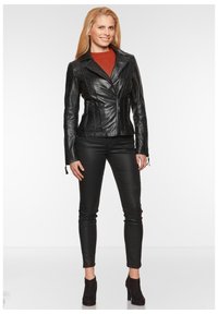 Schwarze Lederjacke mit taillierter Passform, Reverskragen und auffälligen Nähten. Kombiniert mit schwarzen, enganliegenden Hosen und Stiefeletten.