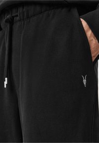 Czarne dresy wykonane z miękkiego materiału, z elastycznym pasem i małą szaro-czarną czaszką umieszczoną na lewej kieszeni.