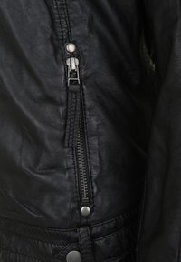 Schwarze Lederjacke mit einem hervorgehobenen Reißverschluss auf der Vorderseite, Metall-Druckknöpfen und strukturiertem Nähen am Saum.