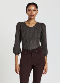 Maglione a trecce marrone scuro con maniche corte a sbuffo, abbinato a jeans marroni aderenti. Texture liscia con dettagli a coste sui polsini.