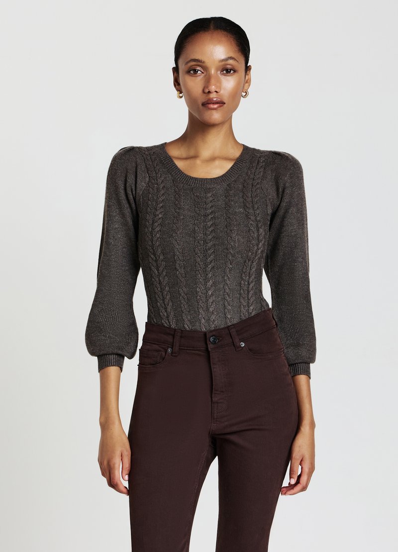 Maglione a trecce marrone scuro con maniche corte a sbuffo, abbinato a jeans marroni aderenti. Texture liscia con dettagli a coste sui polsini.