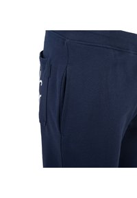 Granatowe dresy z miękkiego materiału, z boczną kieszenią i elastycznym pasem. Na nogawce znajduje się biała nadrukowana logo.