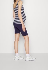 Těhotenský top na ramínka s námořnicky modrými a bílými vodorovnými pruhy, kombinovaný s námořnicky modrými cyklistickými šortkami a stříbrnými teniskami. Hladká látka, přiléhavý střih.