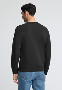 Svart sweatshirt med rund hals och långa ärmar. Har en strukturerad tyg och en åtsittande midja. Bärs med blå denimjeans.