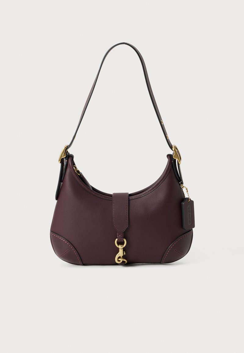Borsa a spalla in pelle viola scuro con chiusura dorata, tracolla regolabile con fibbie dorate e etichetta nera attaccata su uno sfondo bianco.