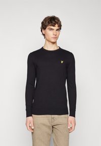 Maglione lavorato a maglia nero con maniche lunghe e colletto a coste. Presenta un piccolo logo giallo sul petto. Tessuto testurizzato e design aderente.