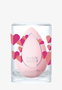 Rosa makeup-svamp i tårform, visad i en genomskinlig cylindrisk behållare med rosa och röda hjärt-grafik på sidorna.