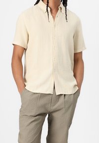 Kortærmet skjorte i lyst beige ribbet stof med knappet krave og afslappet pasform, kombineret med teksturerede khakibukser.