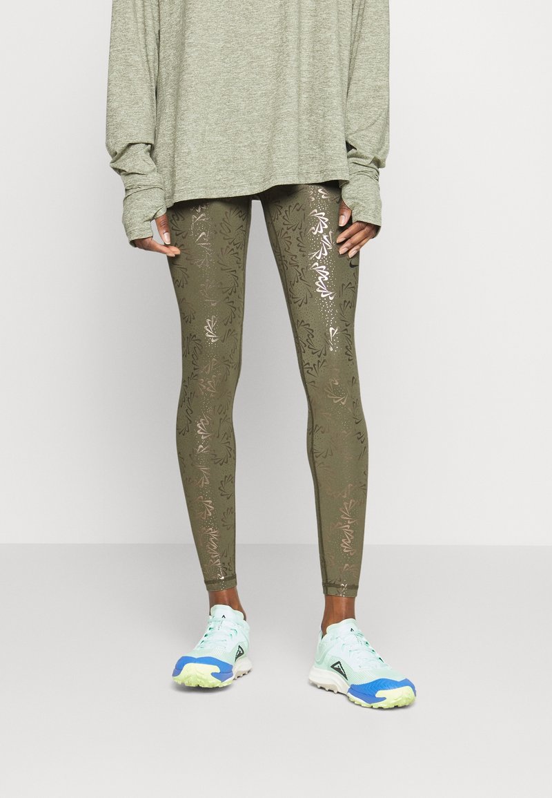 Oliwkowe legginsy z metalicznymi wzorami liści, w połączeniu z jasnobłękitnymi i białymi trampkami. Całość uzupełnia przewiewny szary top w dużym rozmiarze.