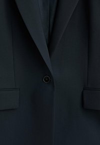 Blazer bleu marine foncé à un bouton avec revers crantés et poches à rabat, présenté en gros plan.