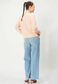 Vaaleanpunainen neulepaita, jossa on kuvioidut hartiat, yhdistettynä korkeavyötäröisiin, löysiin vaaleansinisiin farkkuihin ja ruskeisiin korollisiin sandaaleihin.