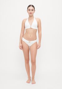 Hvit bikini-sett med halterneck-top med en sentral metalldetalj, og matchende lavt liv bukser med lignende detalj. Glatt tekstur.