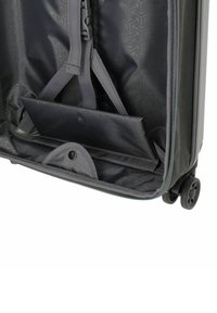 Intérieur de valise noire ouverte avec des sangles ajustables, un compartiment rembourré pour ordinateur portable et deux roues visibles sur le côté.
