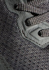 Svart sportskor i närbild med texturerat syntetiskt material, platta snören och en slät tådel som accent.