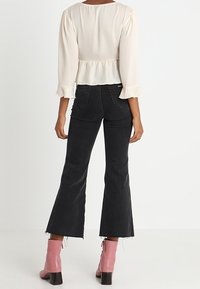 Vit långärmad topp med peplummidja, parat med högmidjade svarta utsvängda jeans och rosa ankelstövlar.