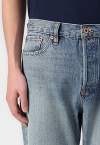 Svijetloplave traperice ravnog kroja, s bakrenim zakovicama, zatvaranjem na gumb i suptilnom izblijedjelom teksturom.