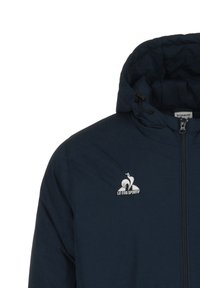 Giacca blu navy con zip frontale, cappuccio regolabile e logo bianco. Texture liscia senza motivi visibili o accenti aggiuntivi.