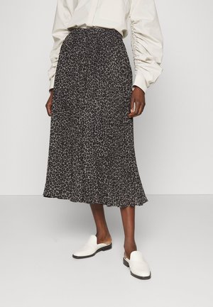 Kvinde iført sort og grå leopardmønstret midi-nederdel, hvid bluse med puffede ærmer og hvide flade slip-on sko.