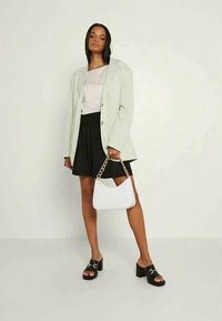 Šviesiai pilkas švarkas ant šviesaus viršaus, juoda plisėta sijonas, juodi aukštakulniai batai ir balta rankinė su auksine grandinėlės dirželiu.