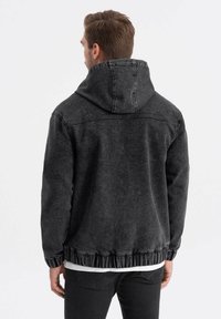 Giacca nera con cappuccio realizzata in denim, caratterizzata da una vestibilità comoda, orlo e polsini a costine, con dettagli cuciti sulle spalle e sulla schiena.