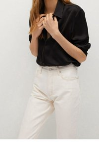 Camisa de seda negra de botones con mangas enrolladas combinada con jeans de mezclilla de cintura alta y de color claro. Diseño simple, sin patrones ni acentos visibles.