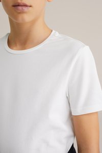 Fehér pamut póló, kerek nyakkal, rövid ujjú, sima tapintású; látható nyakkivágás díszítése részleteket ad.
