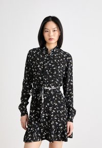 Abito floreale nero con bottini frontali, maniche lunghe e orlo arricciato. Decorato con piccoli fiori blu e gialli, include una cintura da annodare.
