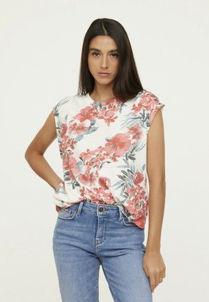 Top sans manches à imprimé floral avec un col rond en beige, orné de fleurs rouges et bleues, associé à un jean bleu. Matière douce et légère.