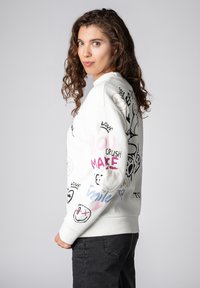 Weißer Pullover mit verschiedenen bunten Grafikdrucken und Texten, locker geschnitten, mit gerippten Bündchen und rundem Ausschnitt.