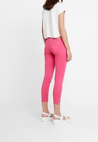 Rosa denimjeans med slim fit och beskuren design, med sidofickor vid fållen; parat med en vit kortärmad topp och platåsandaler.