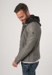 Grijze leren jas met een capuchon, met een aansluitend ontwerp, rits aan de voorkant en zijzakken. Gladde textuur met schouderaccenten.