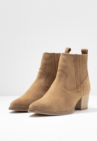 Brązowe zamszowe botki do kostki z zaokrąglonym noskiem, teksturowanymi bocznymi panelami i obcasem na słupku. Wyposażone w pętle ułatwiające zakładanie.