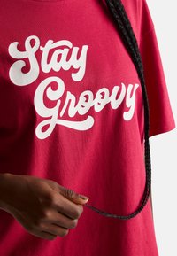 Czerwona bawełniana koszulka z białym, kursywnie napisanym tekstem "Stay Groovy". Krótkie rękawy, luźny krój, gładka tekstura i okrągły dekolt.
