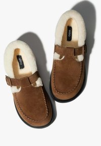 Brązowe zamszowe buty wsuwane z puszystym białym wyściółką, ozdobione dekoracyjną klamrą i detalami przeszyć, z czarną gumową podeszwą.