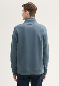 Sweat-shirt bleu clair avec un col montant, des poignets et un ourlet ajustés. Texture lisse, design minimaliste, sans motifs ni accents visibles.