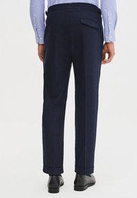 Granatowe spodnie wykonane z teksturowanej tkaniny, z tylną kieszenią i mankietami. Połączone z czarnymi butami i jasnoniebieską koszulą w kratę.