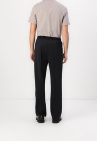 Schwarze, gerade geschnittene Hose mit glatter Textur und Bügelfalten. Kombiniert mit einem hellgrauen Kurzarmhemd und schwarzen Schuhen.