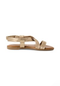 Gold flat sandals with crisscross straps and ankle strap. Smooth metallic finish, brown sole, open toe design, and minimalist styling.