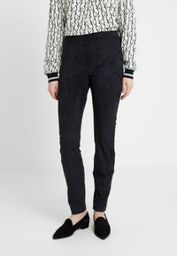 Czarne, dopasowane spodnie z miękkiego, przypominającego zamsz materiału. Wysoka jakość tekstury oraz średnia wysokość pasa. W komplecie z czarnymi butami wsuwanymi.