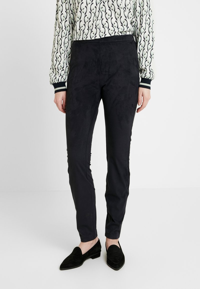 Czarne, dopasowane spodnie z miękkiego, przypominającego zamsz materiału. Wysoka jakość tekstury oraz średnia wysokość pasa. W komplecie z czarnymi butami wsuwanymi.