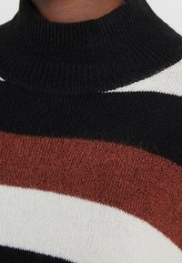 Pruhovaný pletený svetr s vysokým černým límcem. Barvy zahrnují černou, krémovou, vínovou a tenkou bílou pruh. Měkká vlna s příměsí.